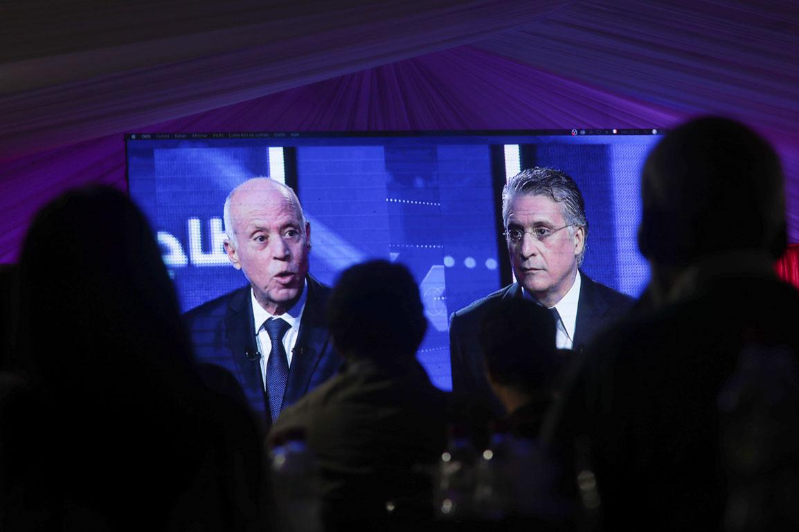 People watch a televised debate between presidential candidates Kais Saied, left, and Nabil Karoui