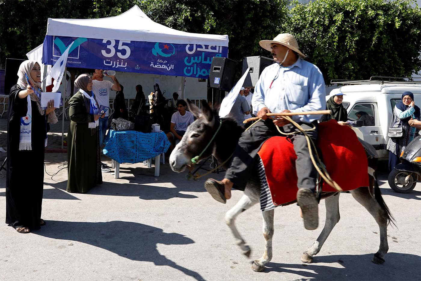A man rides a donkey past a campaign stall of Tunisia's moderate Islamist Ennahda party in al-Alia