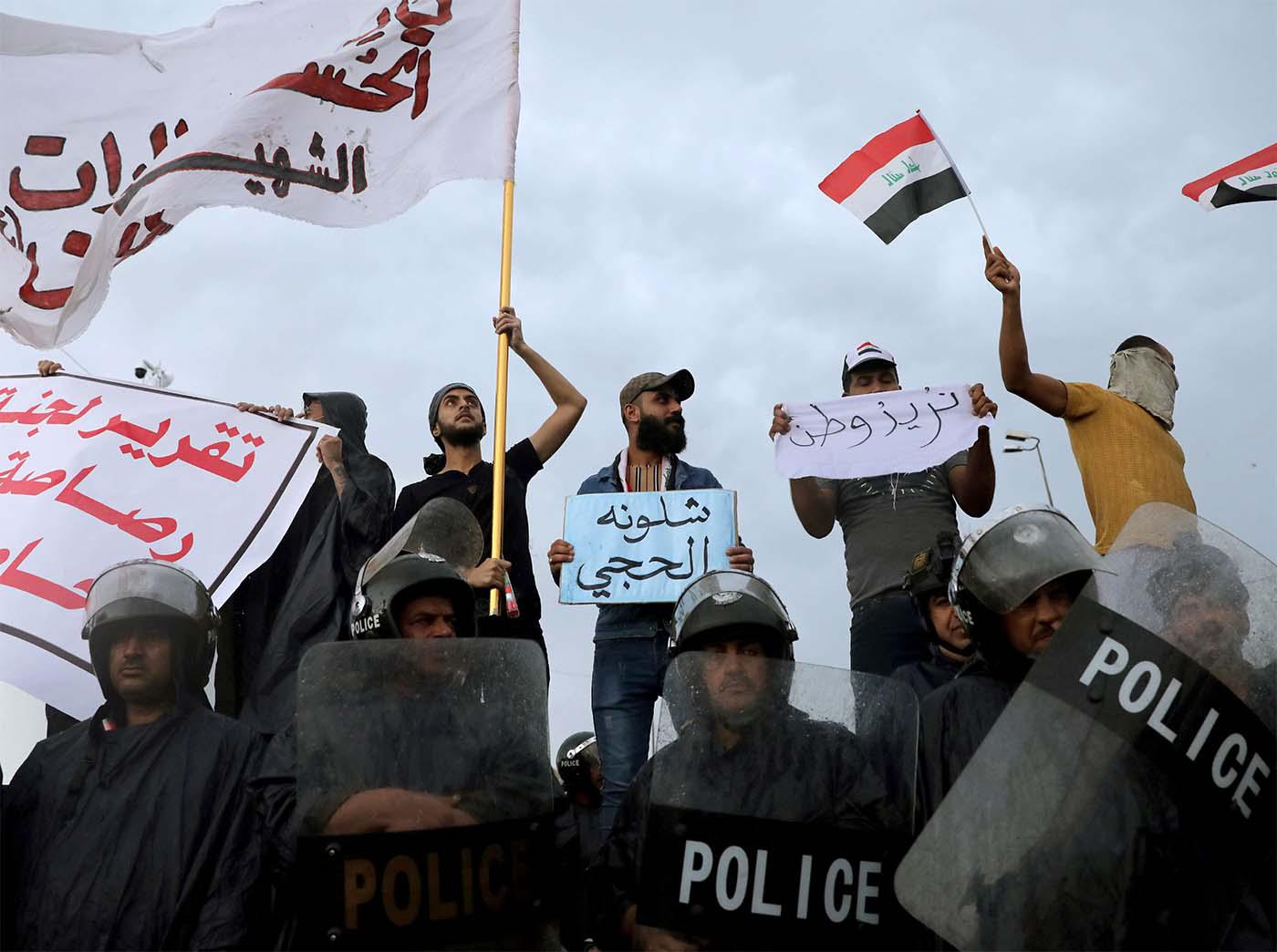raqi policemen stand in front of demonstrators during a protest over corruption, lack of jobs, and poor services, in Kerbala