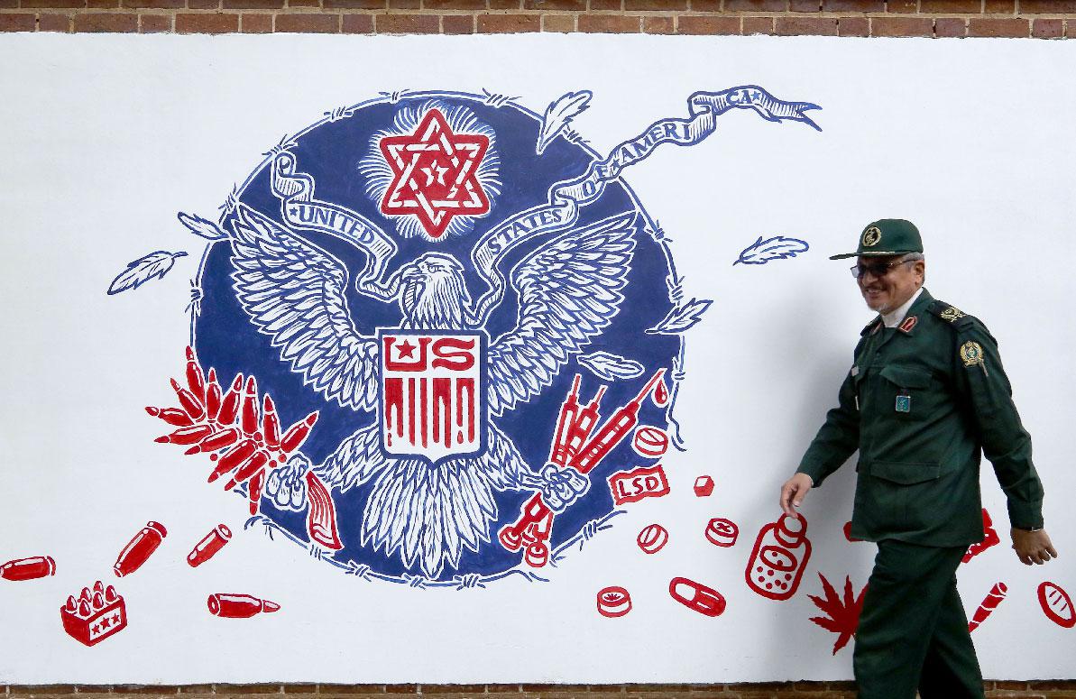 A member of Iran's Revolutionary Guards walks past a new mural painted on the walls of the formar US embassy in the capital Tehran