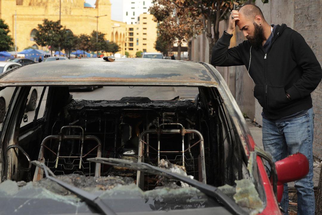 A man inspects the remains of a burned car that was destroyed during clashes between rival groups in Beirut