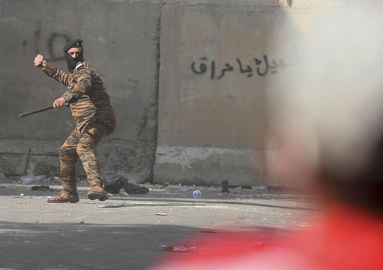 شرطي عراقي يرمي بالحجارة على المتظاهرين في بغداد