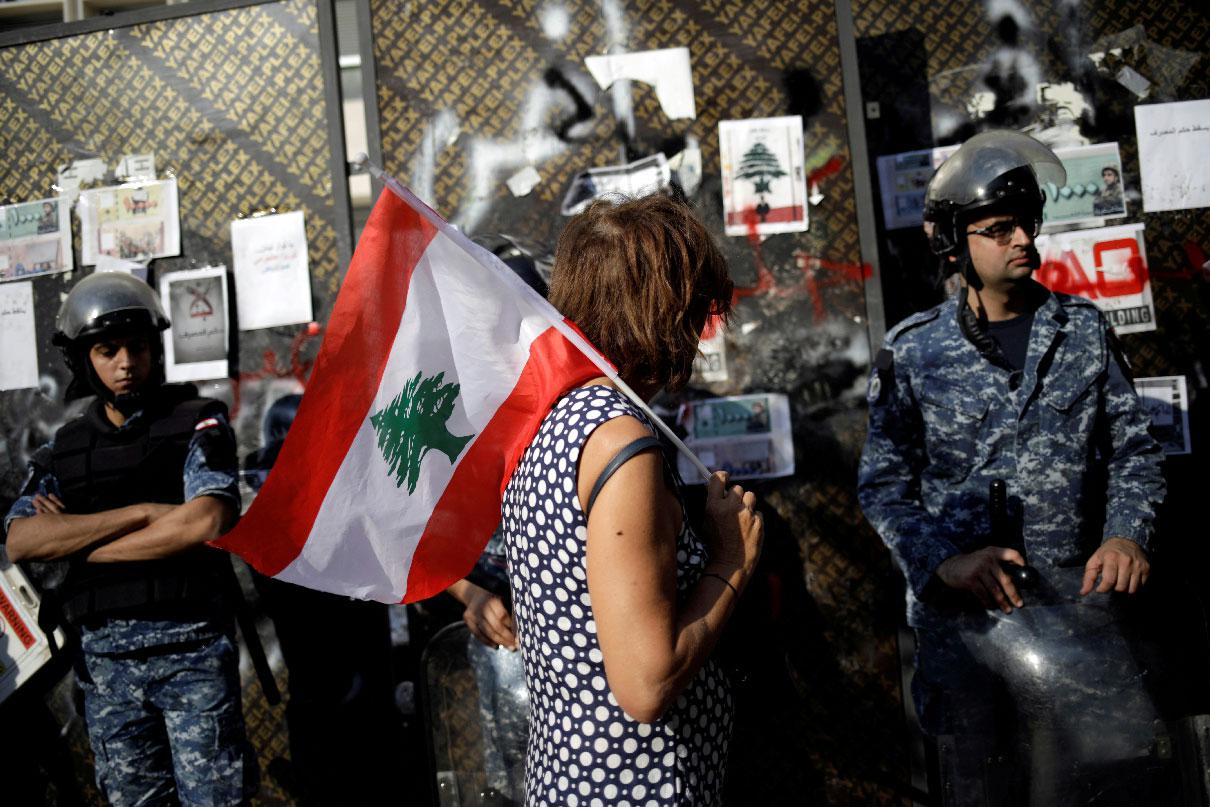 A protester holds a Lebanese flag as she walks in front of police officers