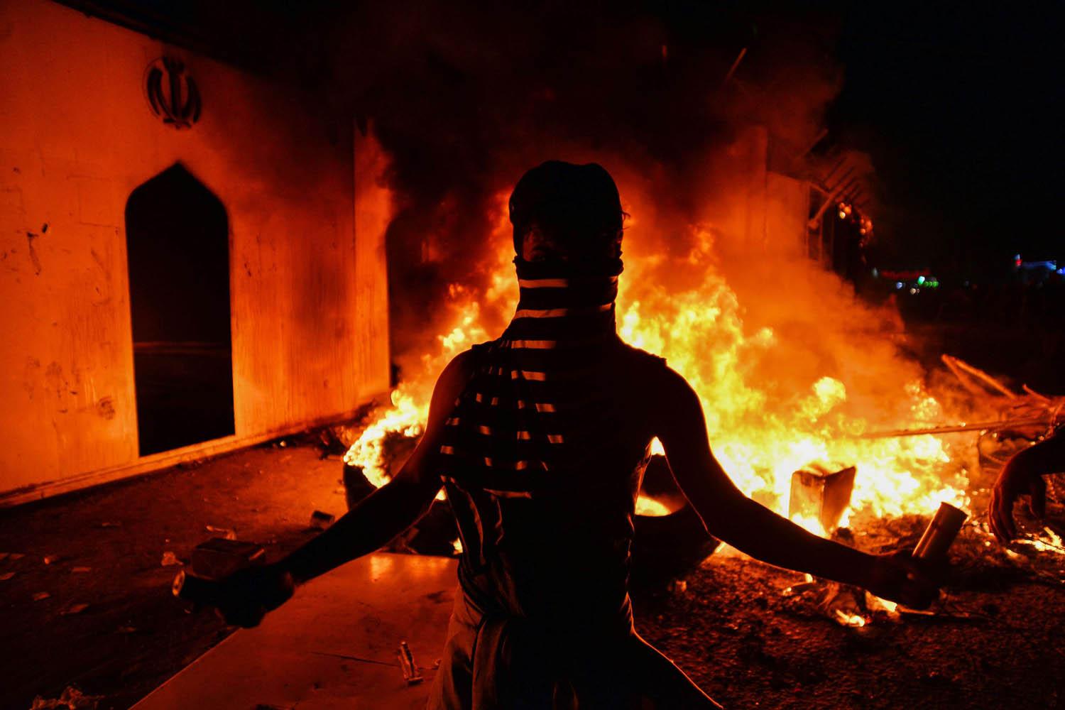 متظاهر عراقي أمام مبنى القنصلية الإيرانية المحترق في النجف
