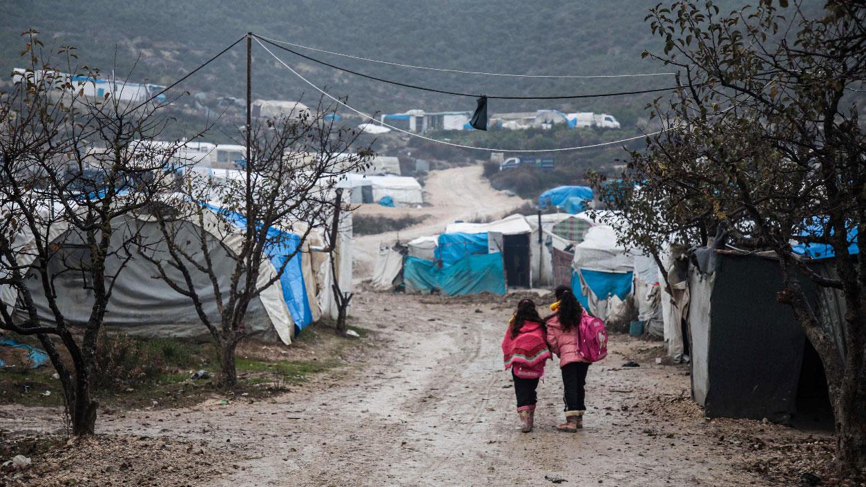 Children walk along a mudpath at a camp for displaced Syrians