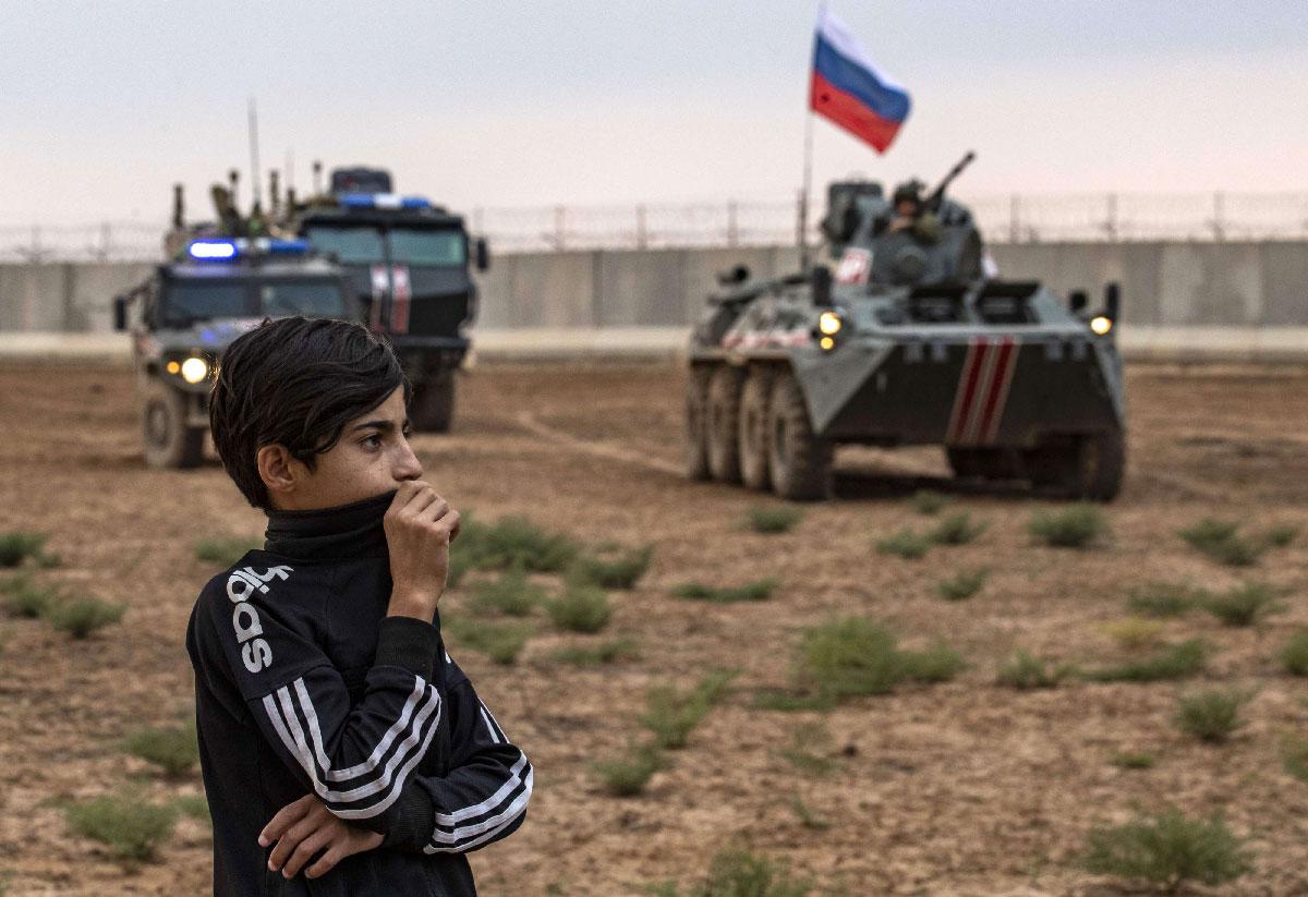 A young boy stands in front of Russian military vehicles in Syria's northeastern Hasakeh province