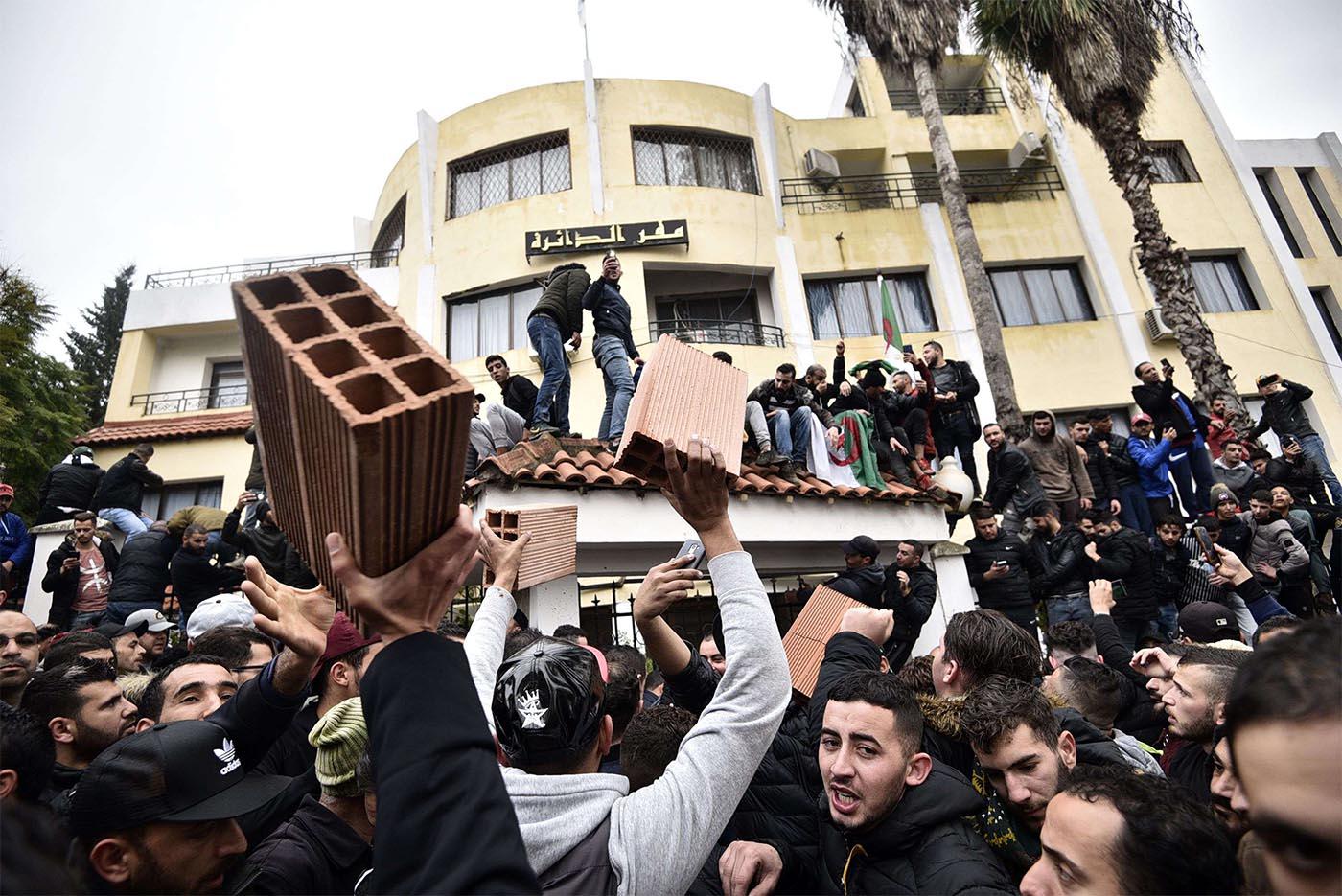Algerian demonstrators carry bricks to build a wall at the entrance of the daira (sub-prefecture) of Tizi-Ouzou
