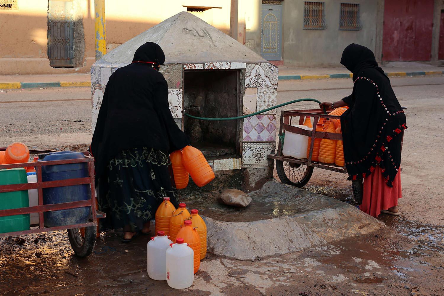 Moroccan women filling up containers with water from a hose in Zagora