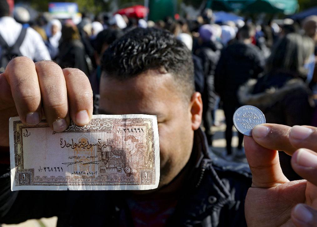 A man shows a Syrian pound in the form of a coin as well as a banknote