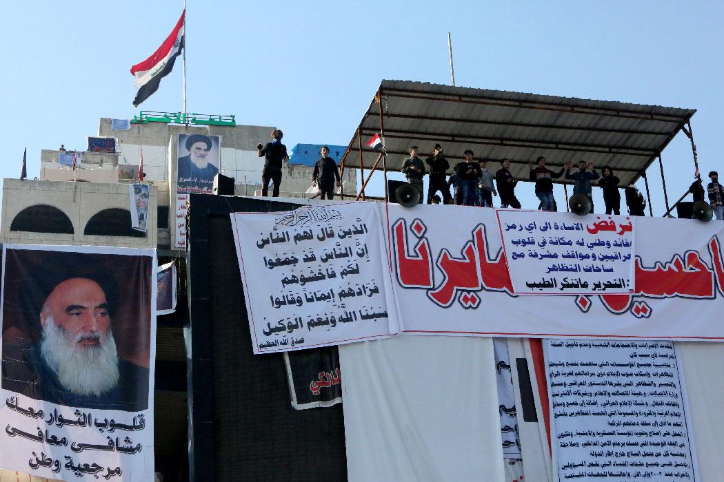 Iraqi anti-government protesters gather on a rooftop with posters bearing images of Grand Ayatollah Ali Sistani