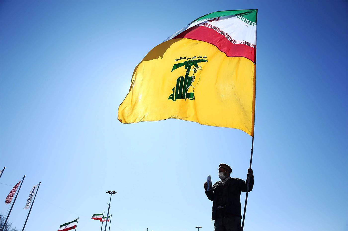 An Iranian carries the Iranian and Hezbollah flags during the commemoration of the 41st anniversary of the Islamic revolution in Tehran