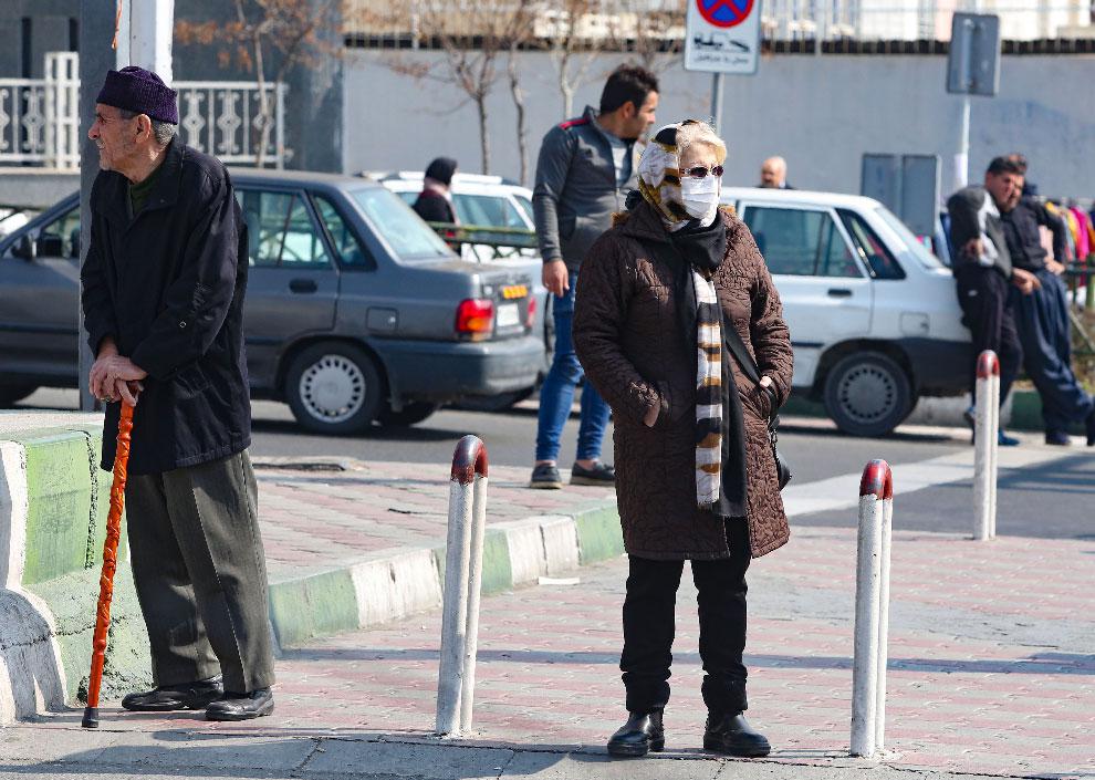 An Iranian woman wearing a protective mask and gloves, stands in a busy street in the capital Tehran