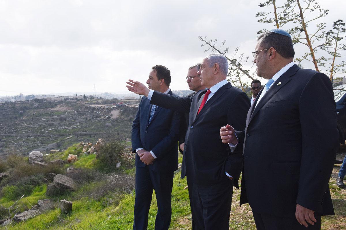 Israeli PM Benjamin Netanyahu (2-R) points from an overview at the Israeli settlement of Har Homa 