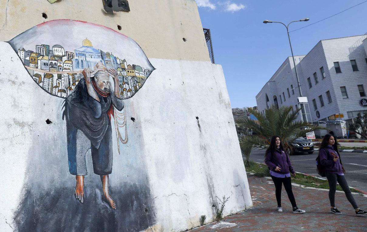 Schoolgirls walk past a mural in the Palestinian town of Umm al-Fahm inside Israel
