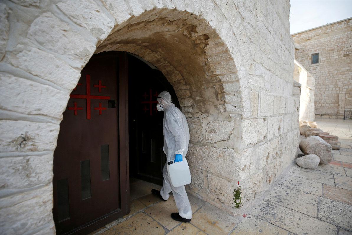 A worker wearing a protective suit arrives to disinfect the Church of the Nativity