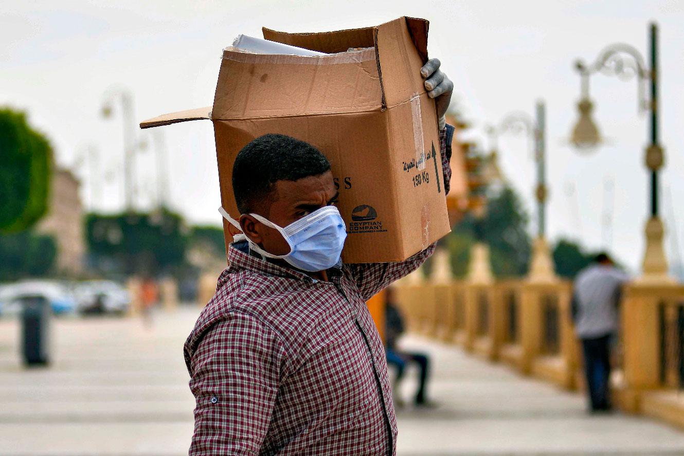A worker on a Nile cruise ship, wearing a protective face mask, walks carrying a box along the corniche overlooking the river bank in Egypt's southern city of Luxor