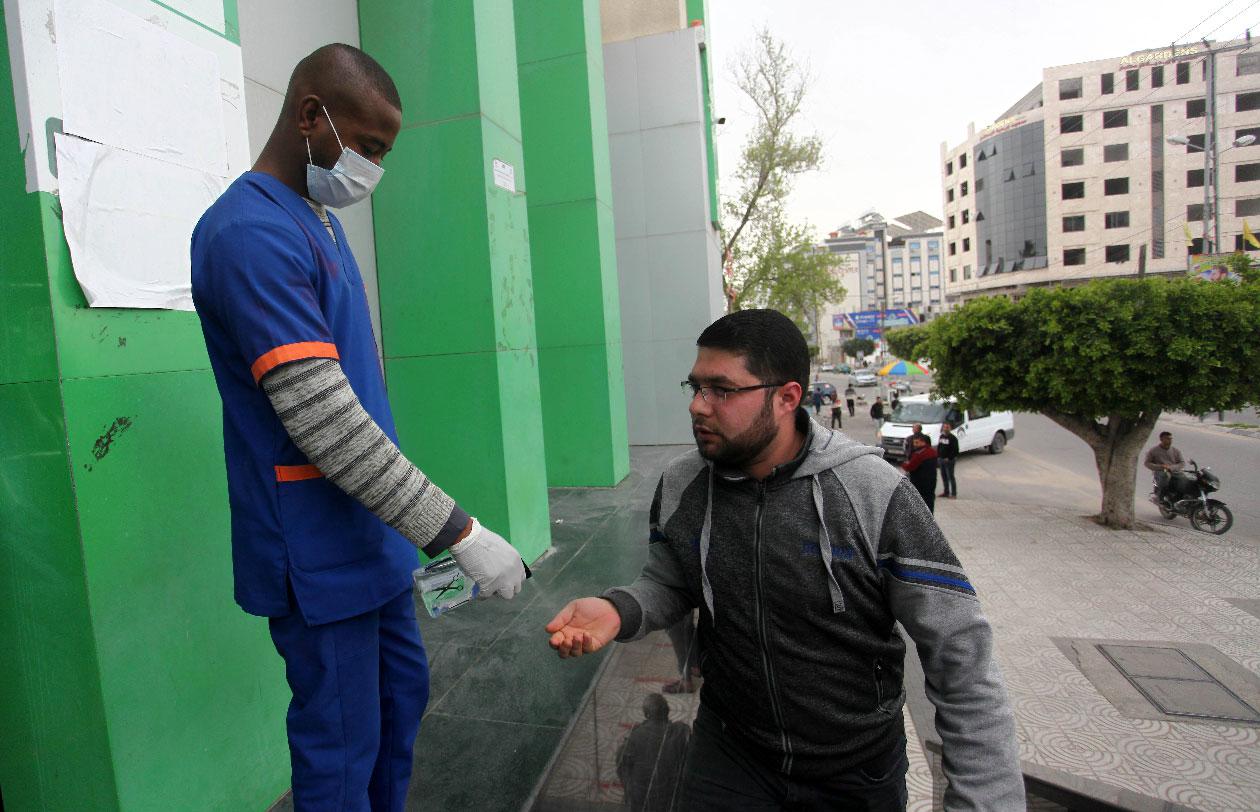 A worker sprays disinfectant on the hands of a Palestinian man at a Post Office in Gaza