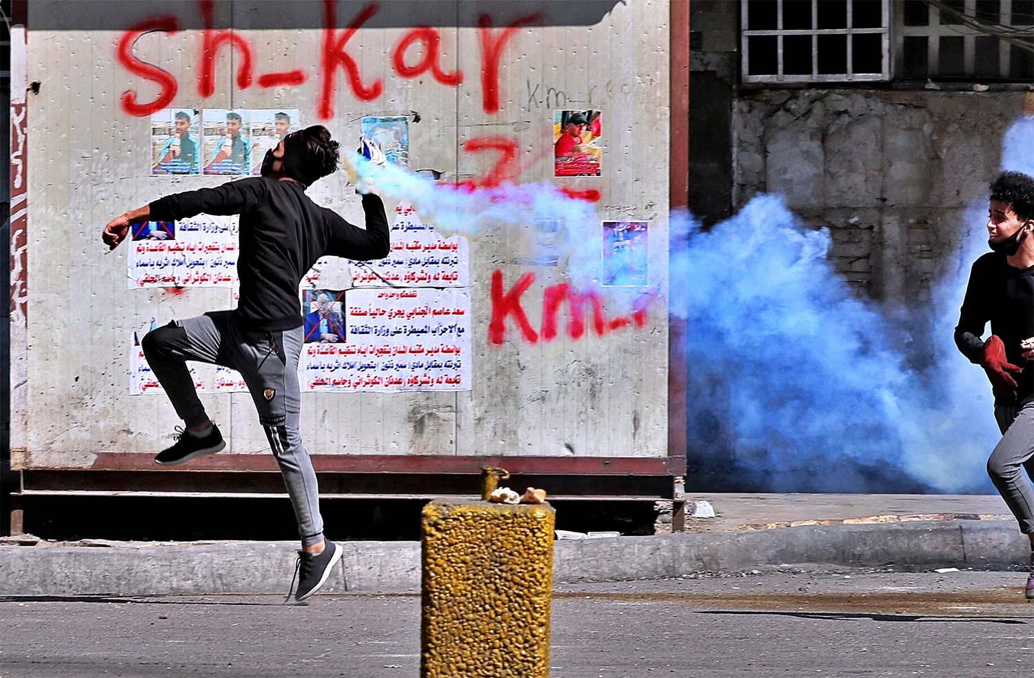 An anti-government protester prepares to throw back a tear gas canister fired by riot police, during clashes in Baghdad 