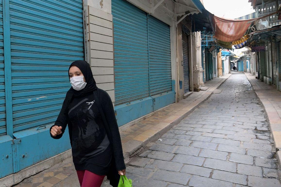 A Tunisian woman wearing a protective face mask walks through an alley in the souk of the Medina