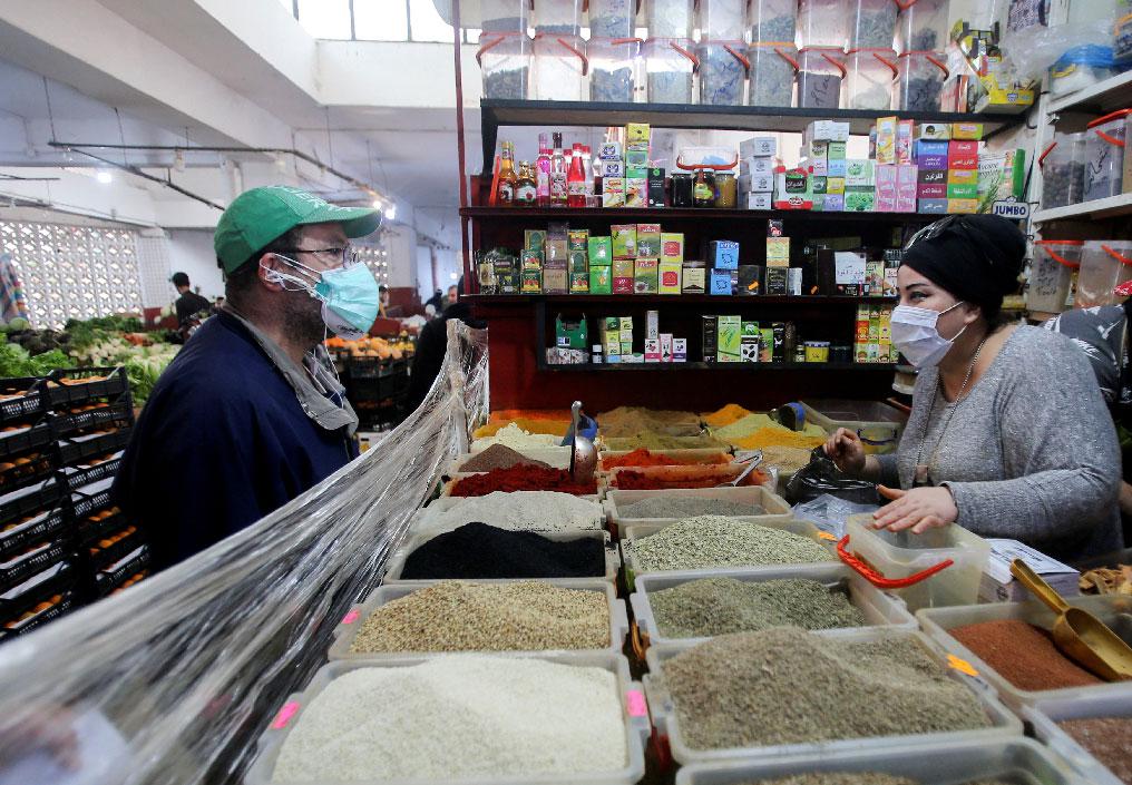 A vendor wearing a protective face mask serves a customer inside her shop in Algiers