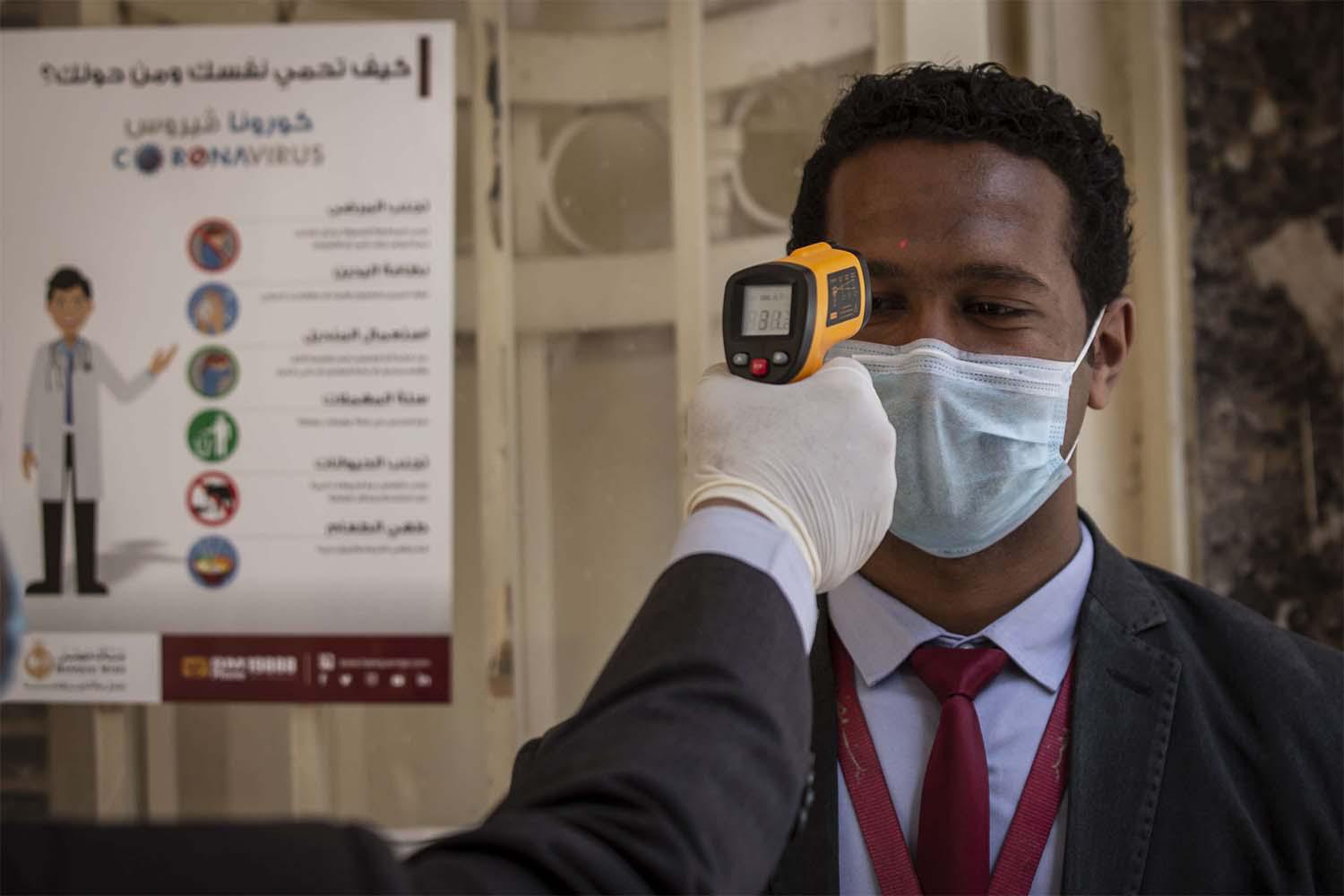 An employee has his body temperature checked before entering the Egyptian bank 'Banque Misr' headquarters