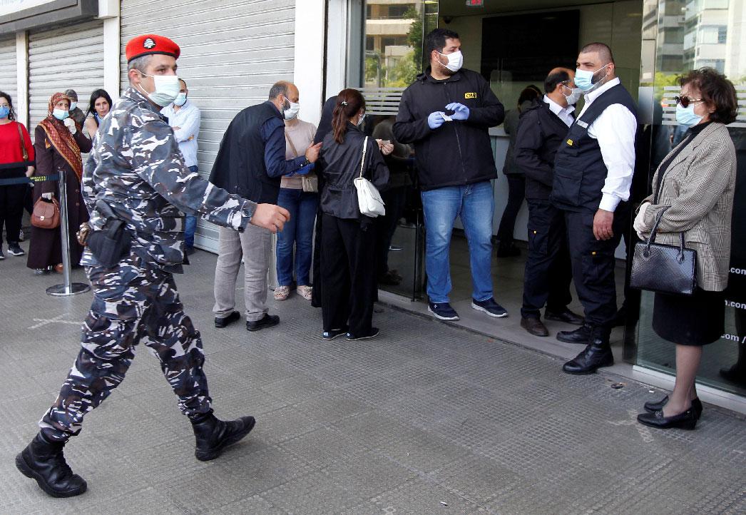 A Lebanese police officer walks near a crowd formed outside a money transfer office