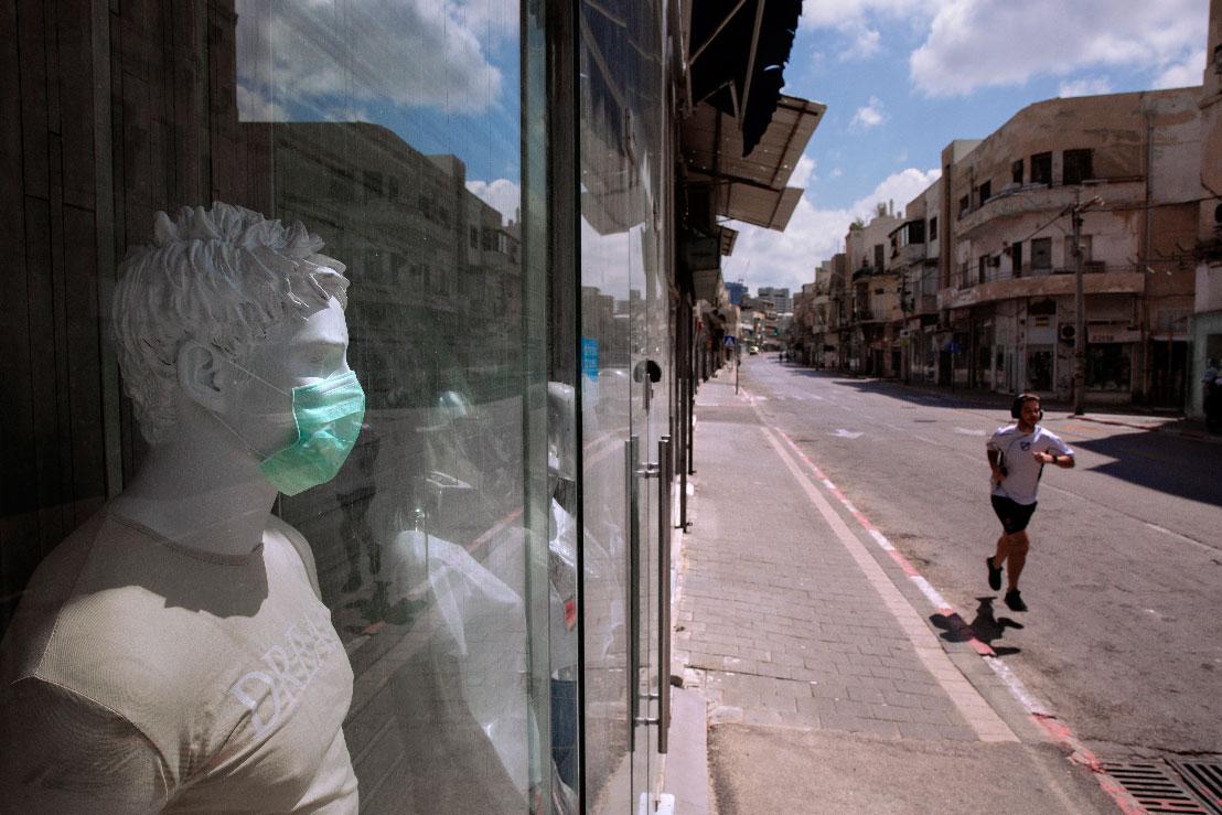 A man runs on an empty street next to a shop in Tel Aviv, Israel