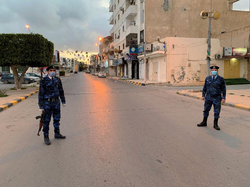 Libyan policemen wearing protective masks, stand guard on a street during a curfew in Misrata, Libya