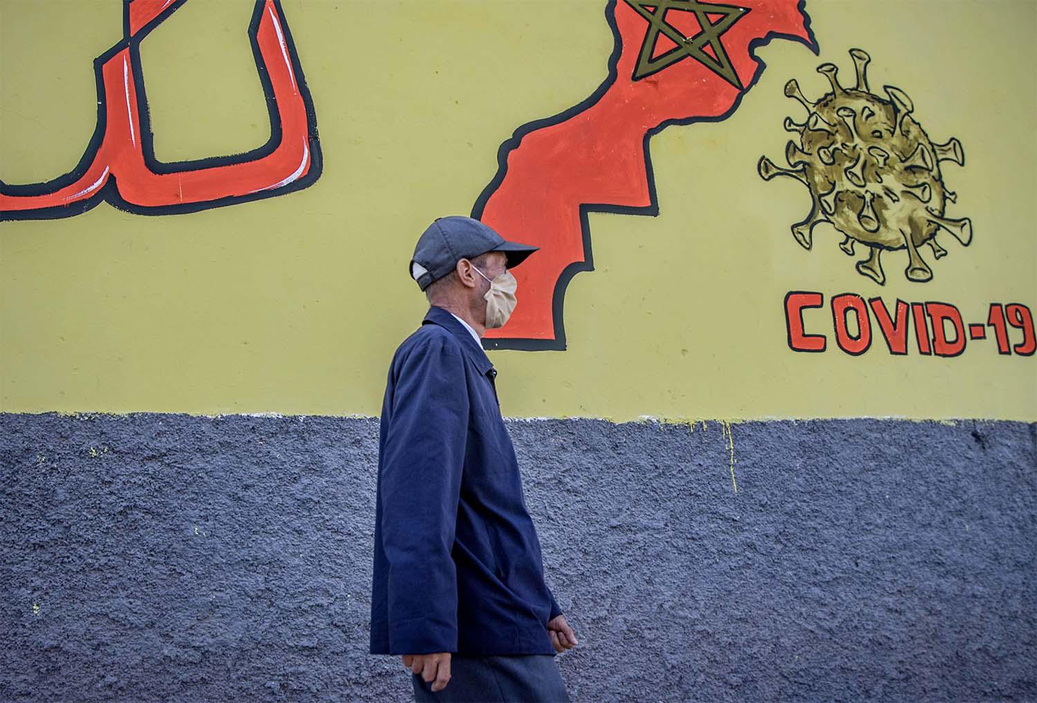 A Moroccan man wearing a protective mask walks past a mural painting of COVID-19