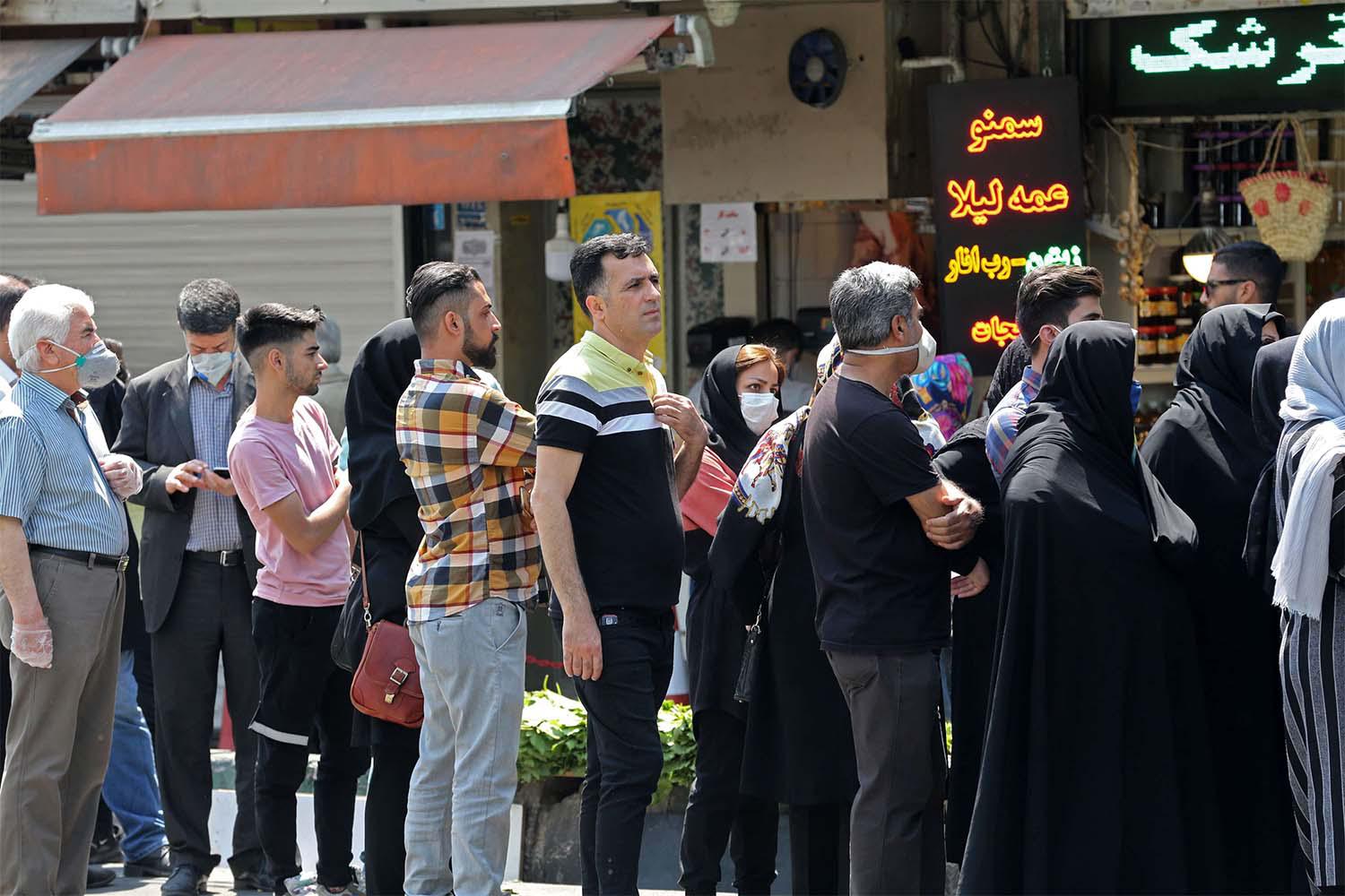 Iranians, wearing protective masks without observing social distancing, queue outside a money exchange office in Tehran
