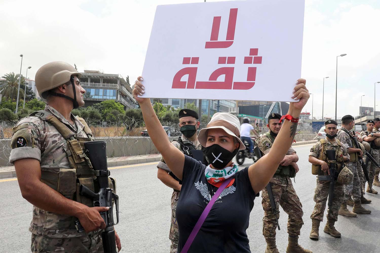 A Lebanese anti-government protester holds a placard reading "No Trust" in front of army soldiers as she takes part in a demonstration near the presidential palace in Beirut
