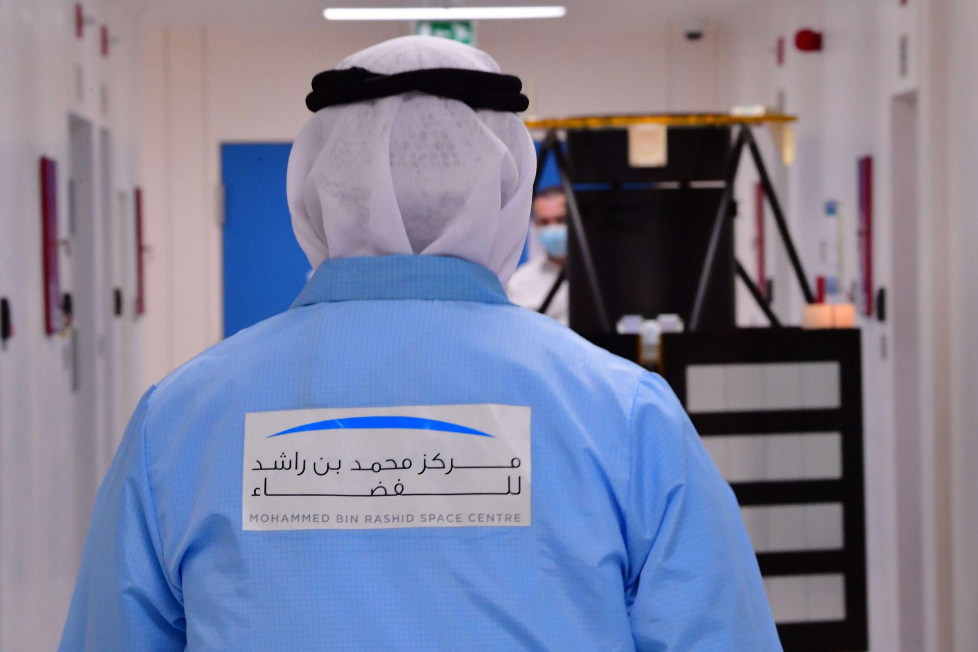 خبير اماراتي يرتدي شعار مركز الشيخ محمد بن راشد للفضاء يسير باتجاه نموذج لخليفة سات