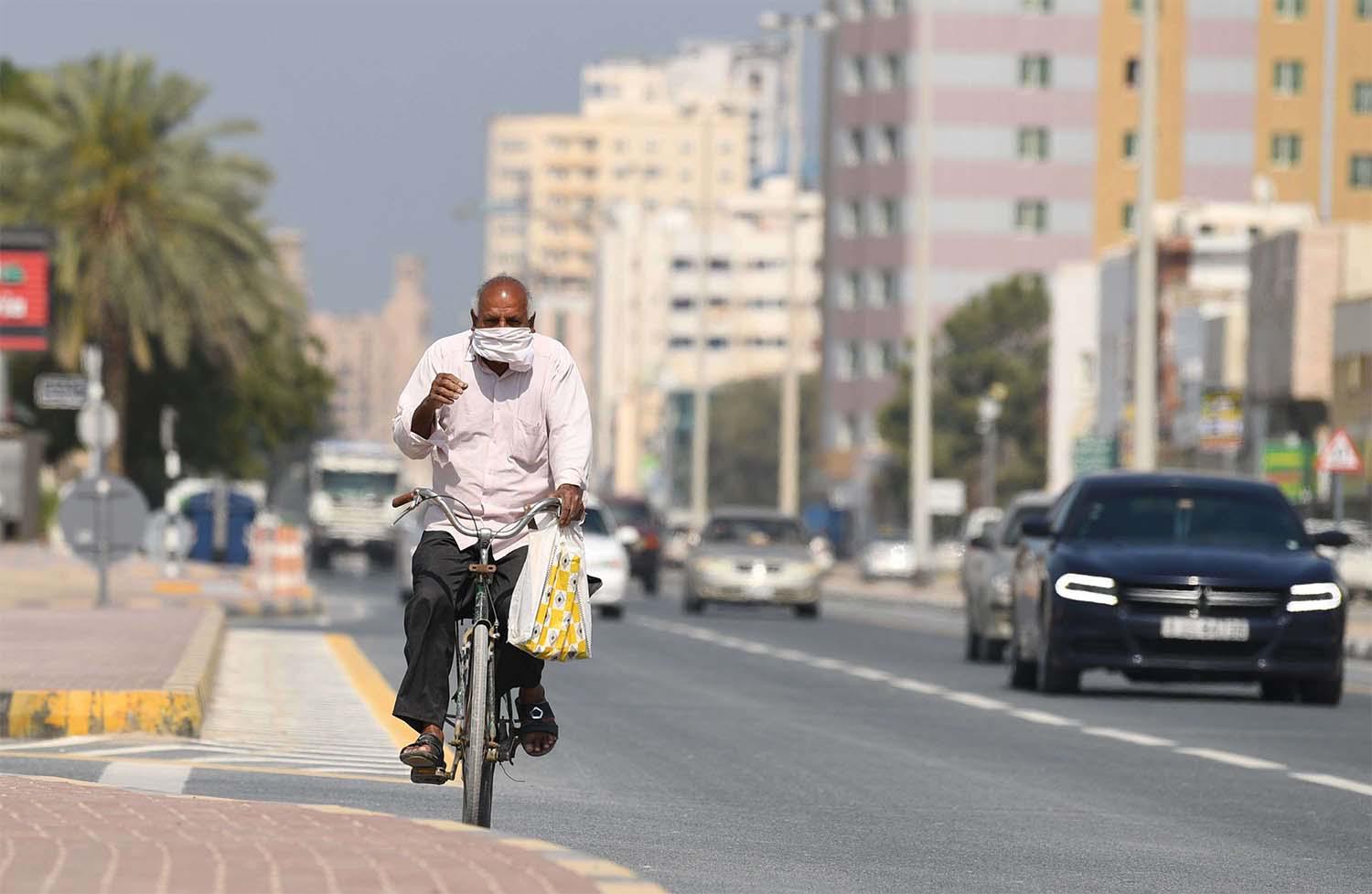 A worker wearing a protective mask bikes on a street in Sharjah