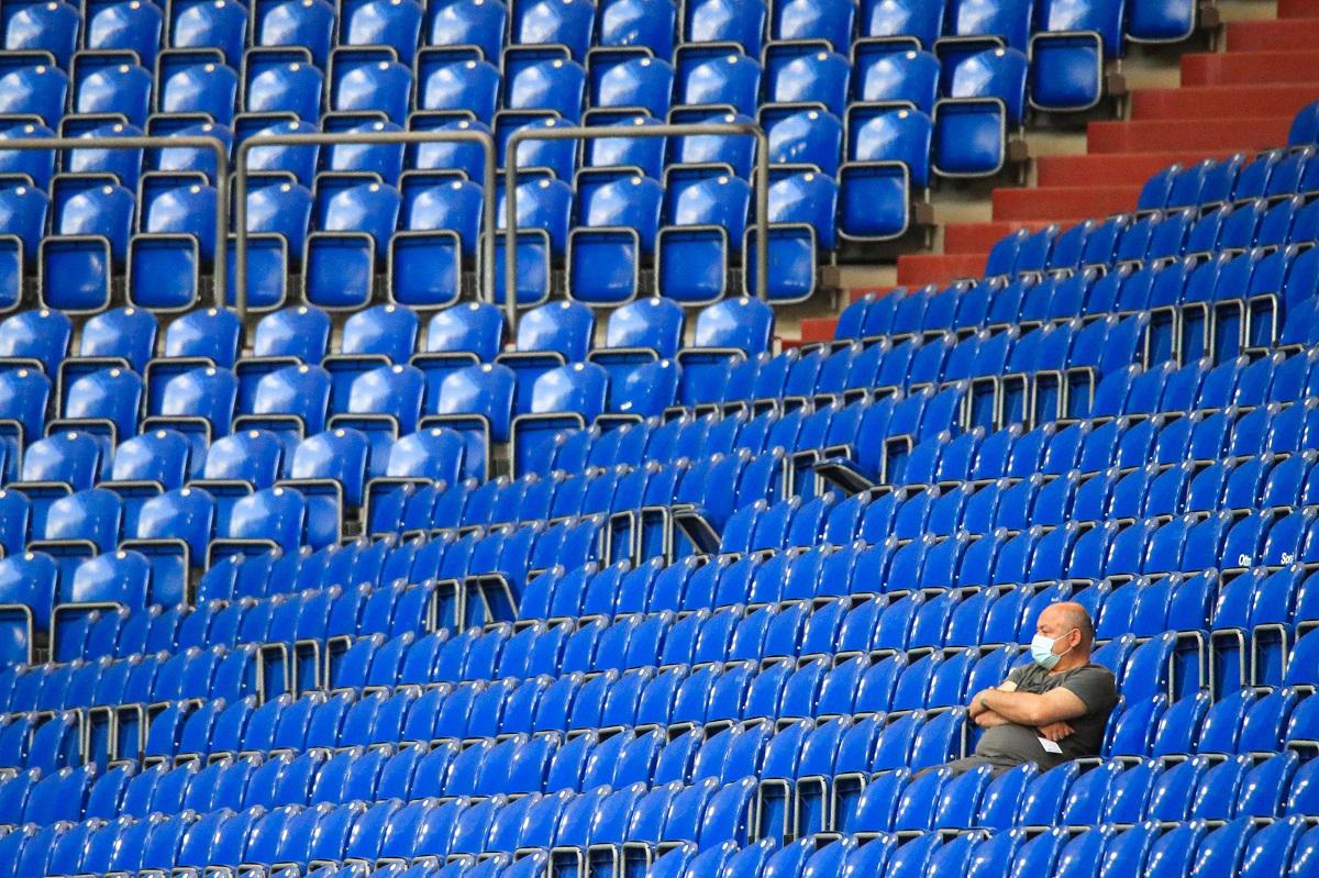 رجل يرتدي كمامة يجلس في ملعب فارغ أثناء حضوره مباراة دوري الدرجة الأولى الألماني لكرة القدم