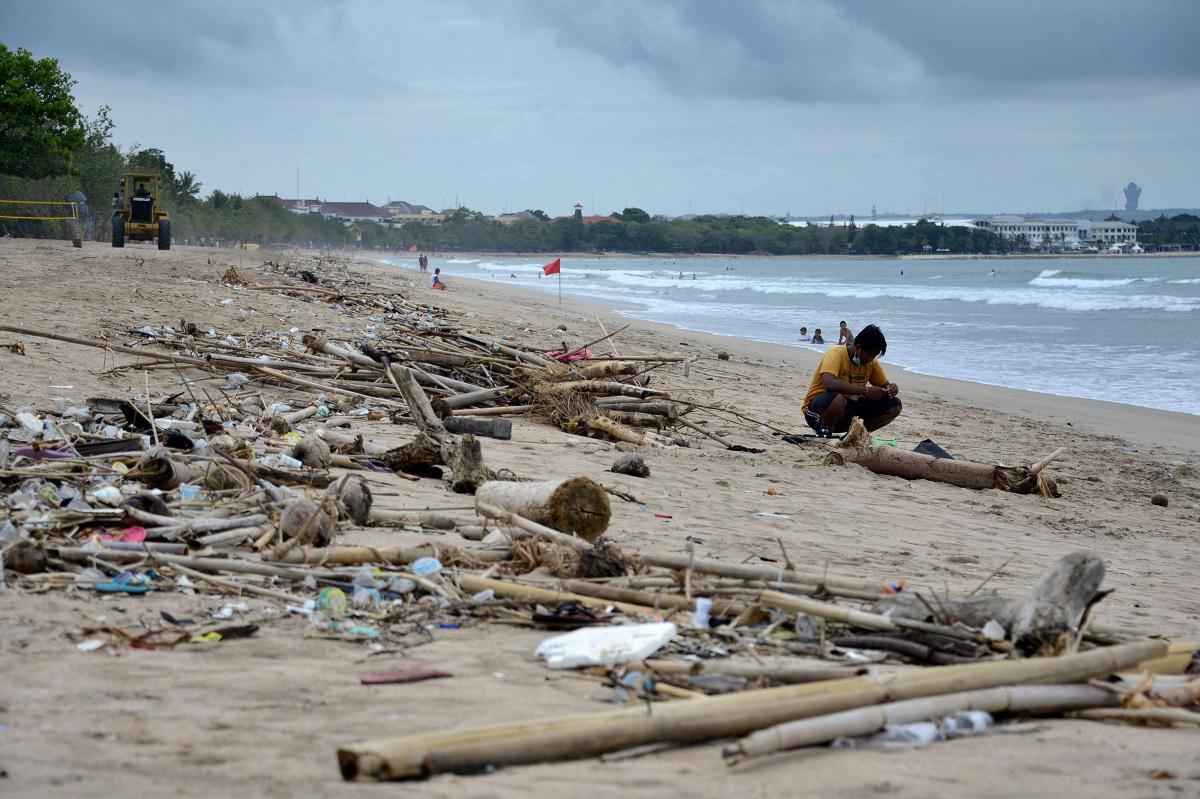 رجل يجلس بالقرب من نفايات بلاستيكية جرفتها الأمواج على شاطئ كوتا في جزيرة بالي الإندونيسية
