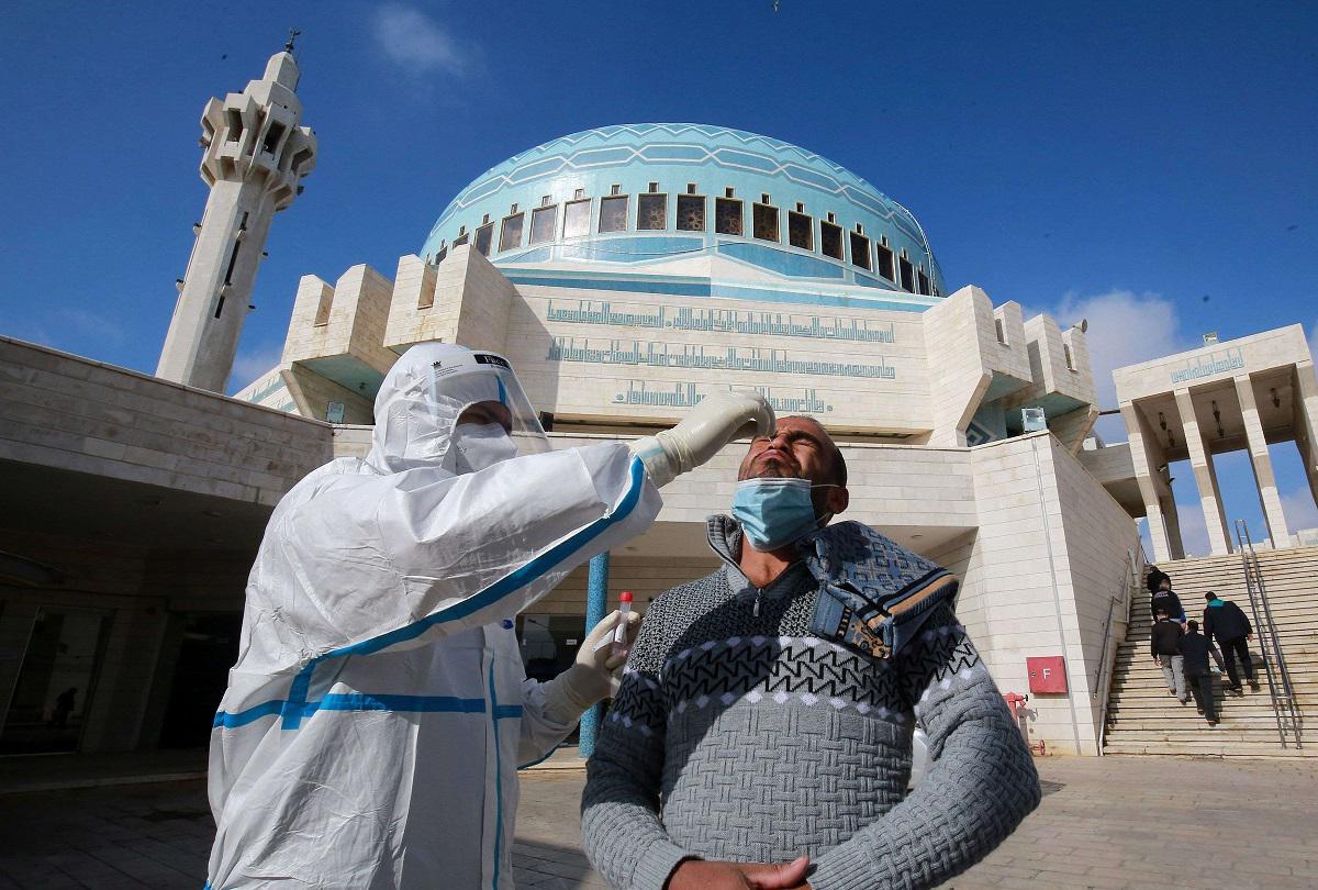 عضو فريق طبي يأخذ مسحة أنف لفحص كورونا، من رجل غادر مسجدا بعد الصلاة في عمّان