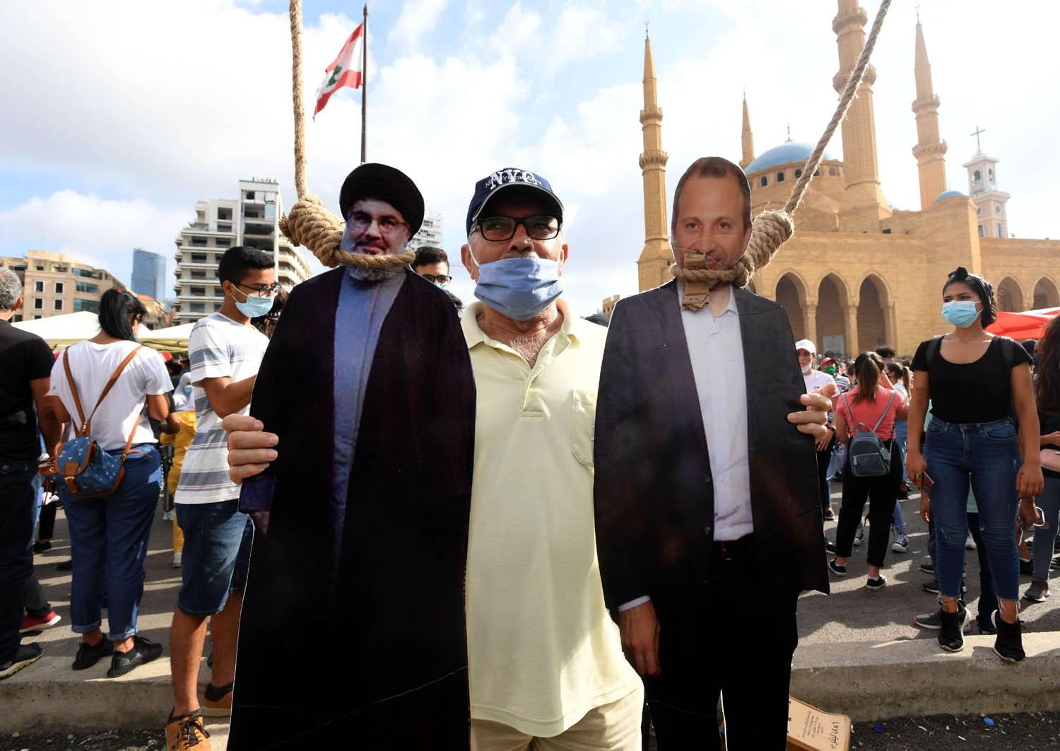 لبناني يرفع صورا معلقة من حبال لجبران باسيل وحسن نصرالله في تظاهرة في بيروت