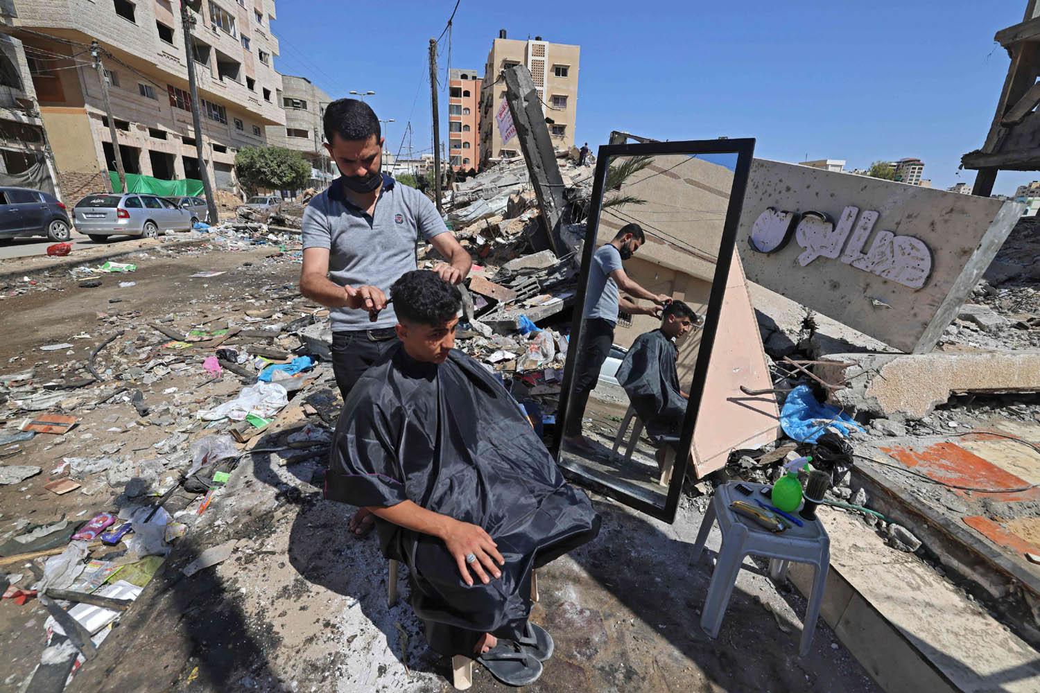 حلاق فلسطيني يعمل أمام ركام دكانه في غزة
