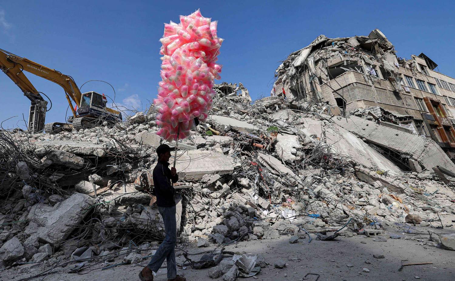 بائع متجول فلسطيني يبيع الحلوى بالقرب من اطلال أبنية مدمرة في غزة