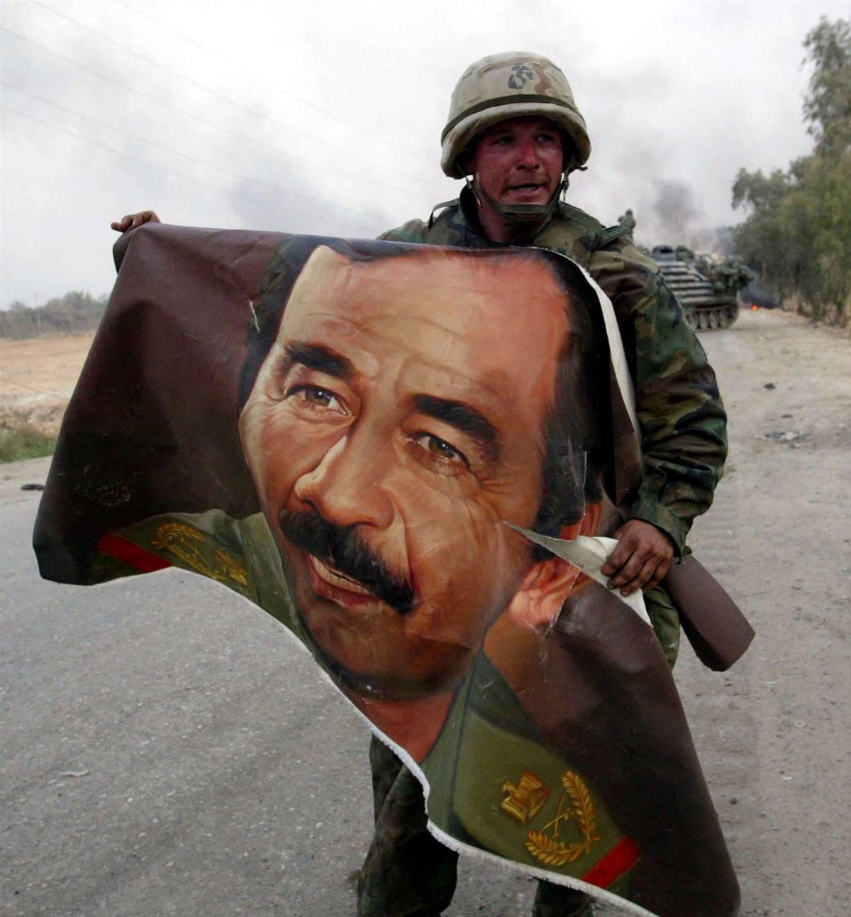 جندي أميركي يحمل صورة للرئيس العراقي الراحل صدام حسين بالقرب من جسر على دجلة جنوب بغداد (2003)