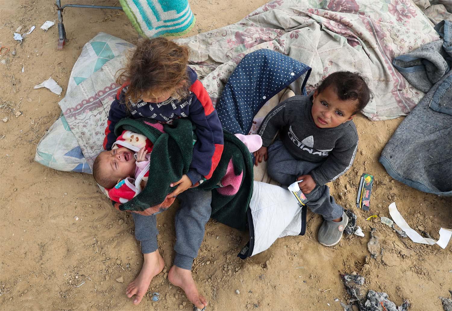 Displaced Palestinian children who fled their houses due to Israeli strikes sit outside as they take shelter in a tent camp in Rafah