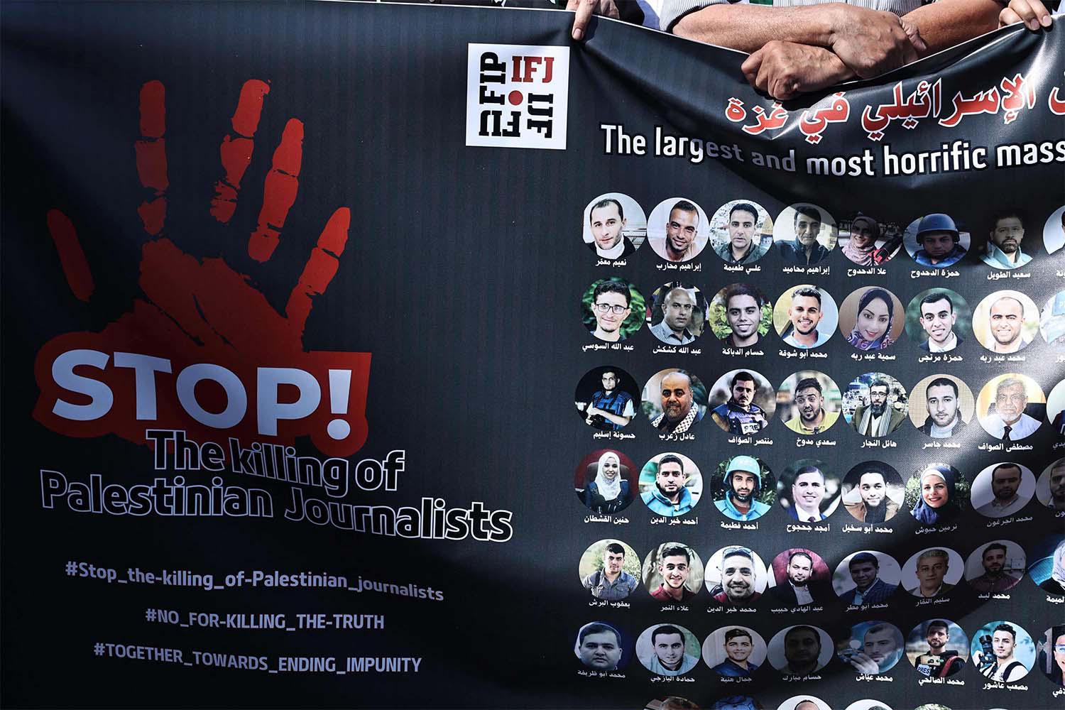 Protesters carry a banner bearing pictures of slain Palestinian journalists during a rally to condemn their killing