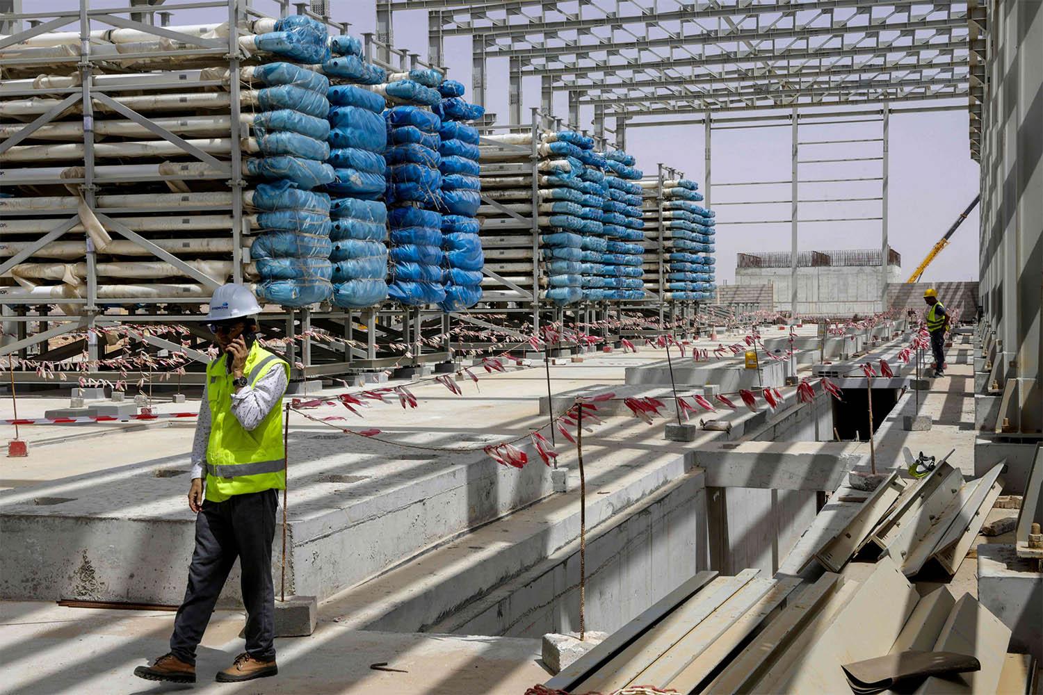 Workers stand near next to heavy equipment during the construction of a desalination plant in Dakhla