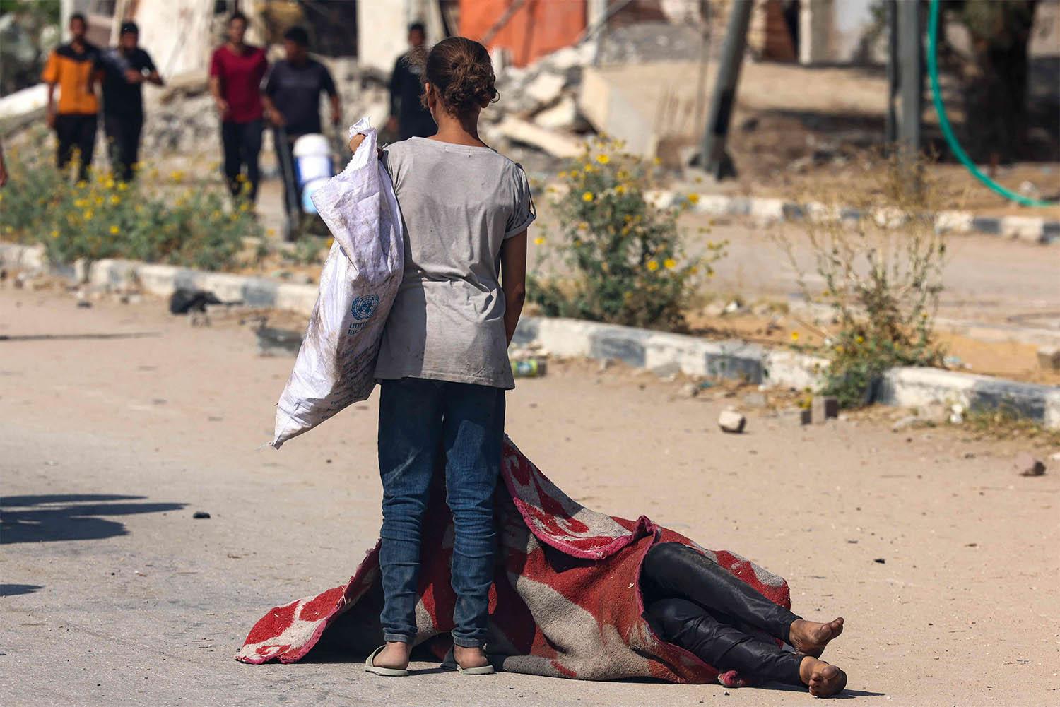A Palestinian girl stands over the covered body of a person who was killed while seeking food at a distribution point run by the US and Israeli-backed Gaza Humanitarian Foundation group, in Nusseirat
