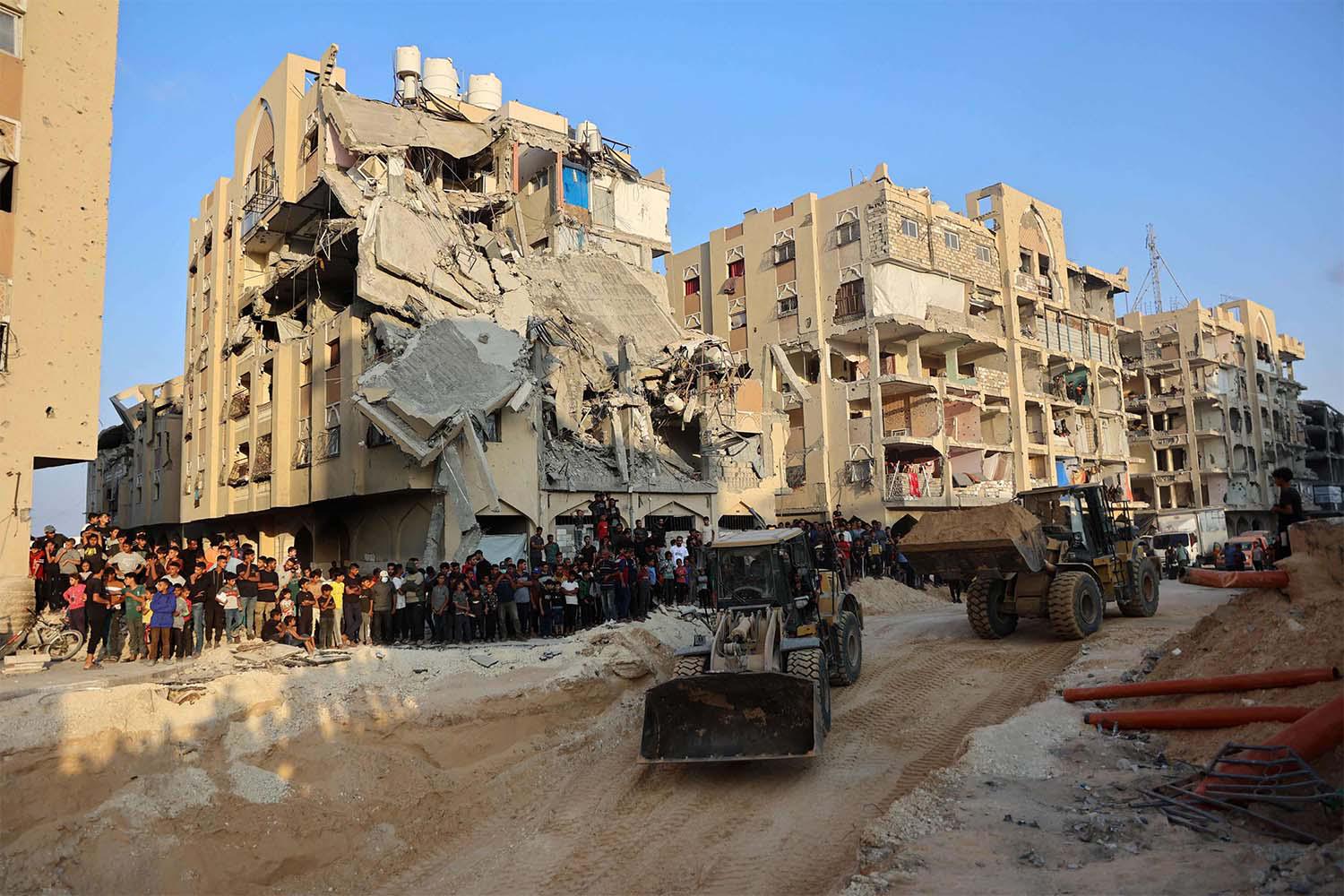 People watch as Palestinians use excavators to dig deep into the ground reportedly searching for bodies in Khan Yunis 