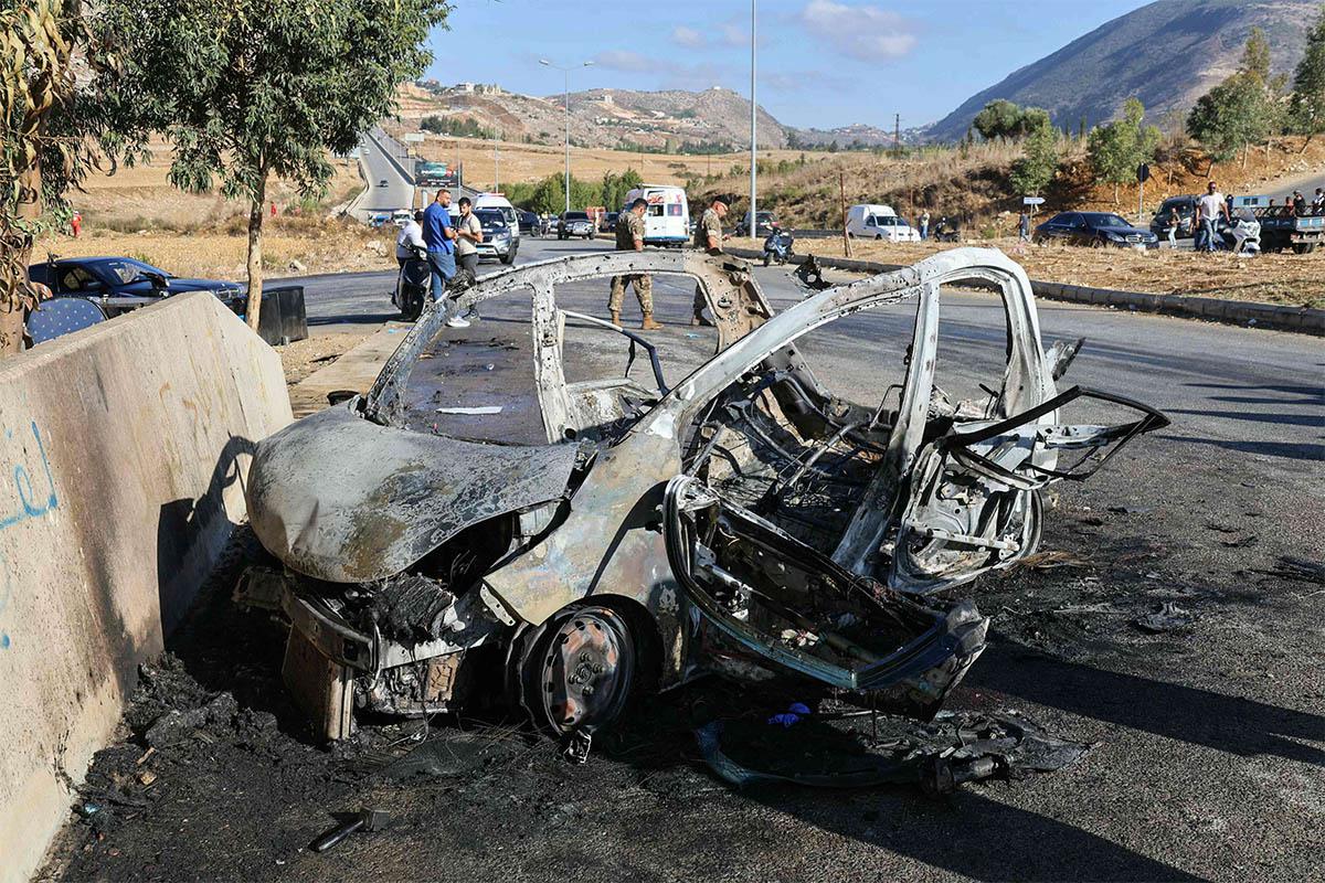 Lebanese emergency and security service members deploy around the wreckage of a car hit by an Israeli drone attack in the southern area of Al-Jarmak 