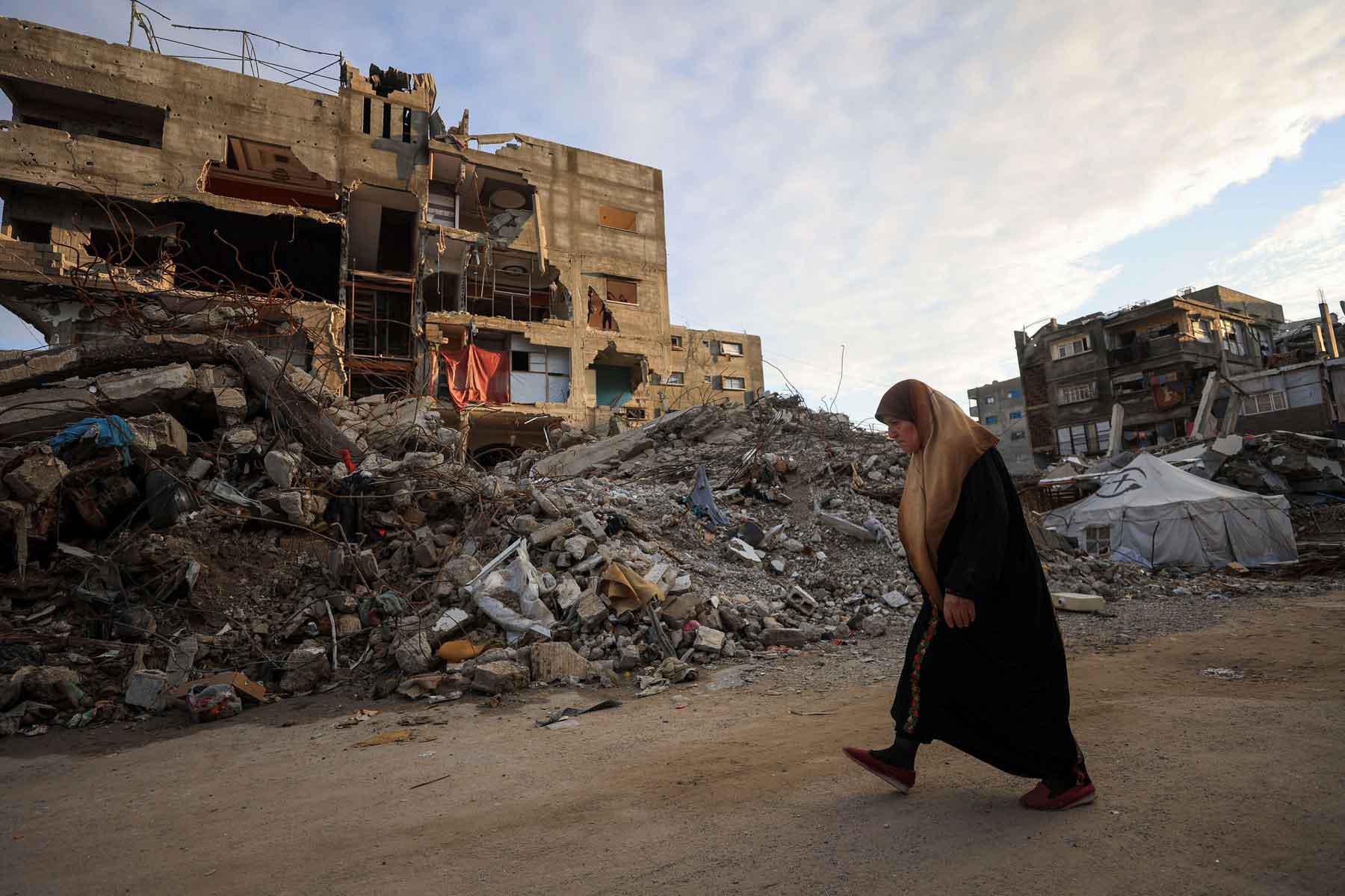 A Palestinian woman walks past residential buildings damaged and destroyed during the war, in Gaza City, December 14, 2025. 