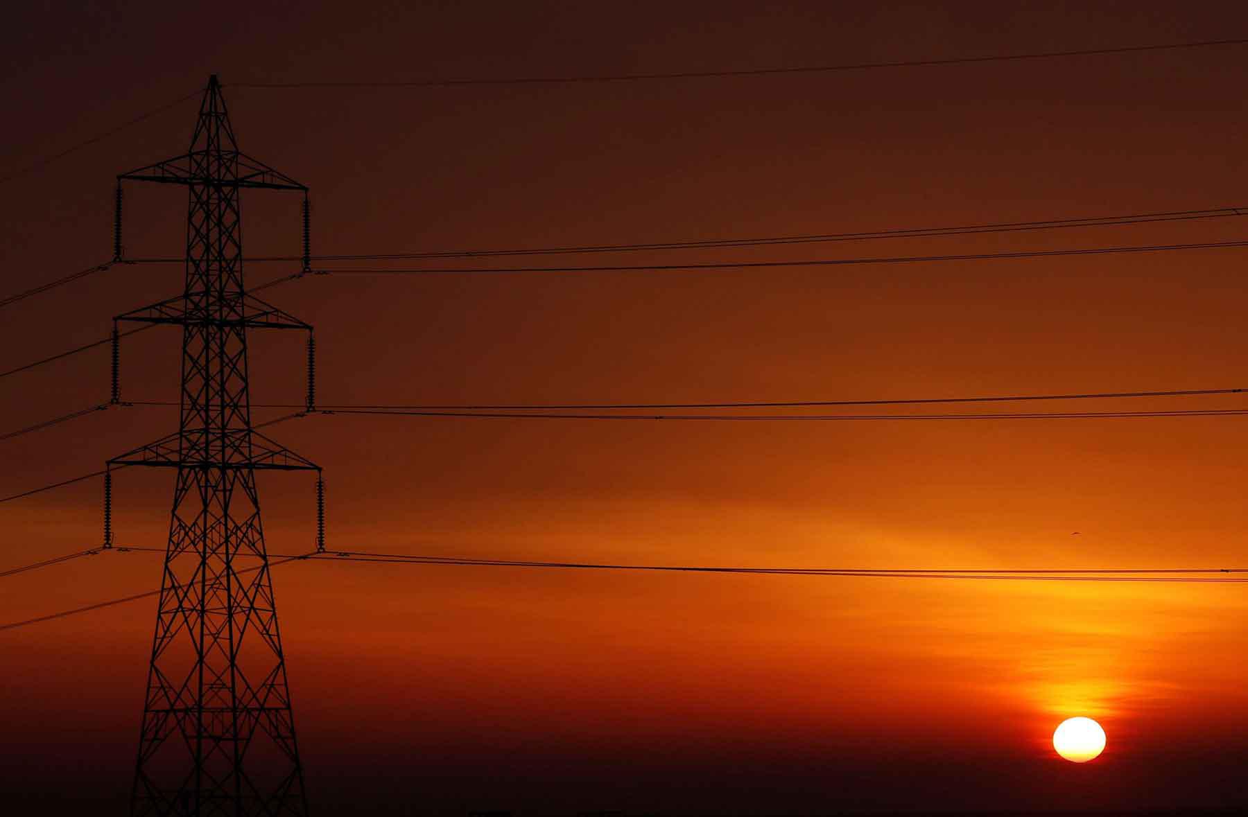 The sun is seen behind high-voltage power lines and electricity pylons at a highway northeast of Cairo.