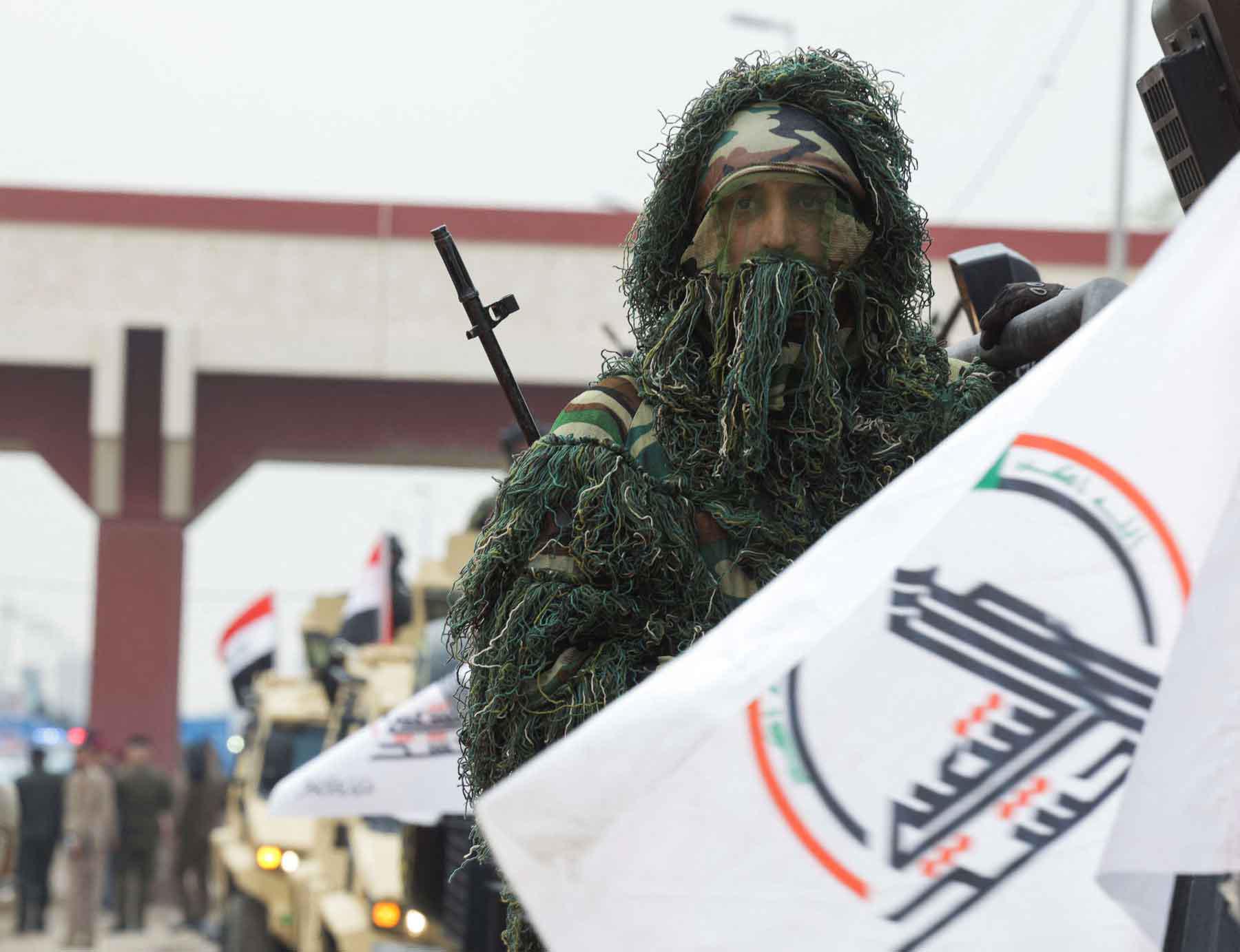 A member of Iraq’s Popular Mobilisation Forces (PMF) rides in a military vehicle next to a flag during a parade in Baghdad, December 10, 2025. 