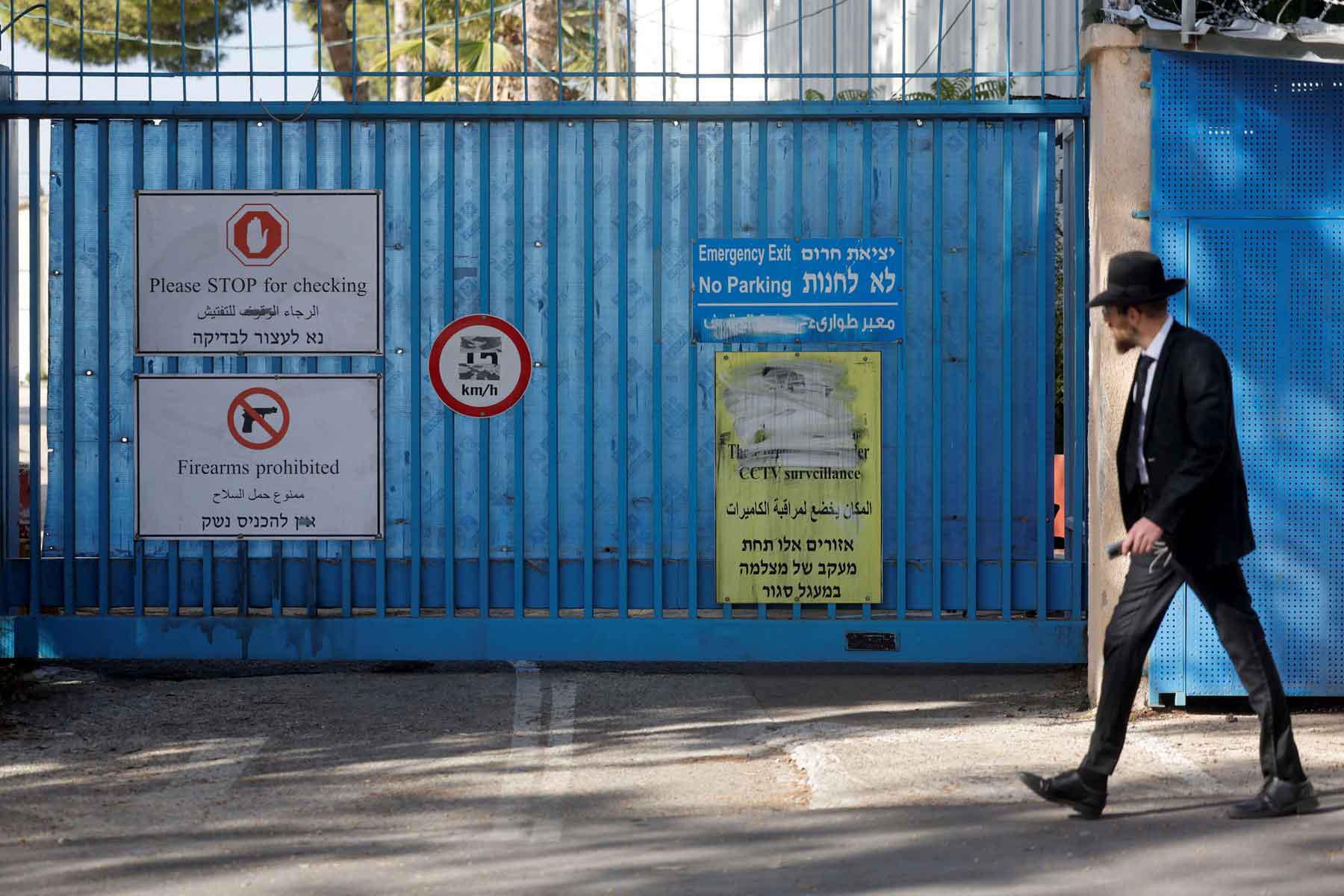 Signs are displayed at the gate of the UNRWA headquarters as a Jewish man walks outside, in Jerusalem December 8, 2025. 